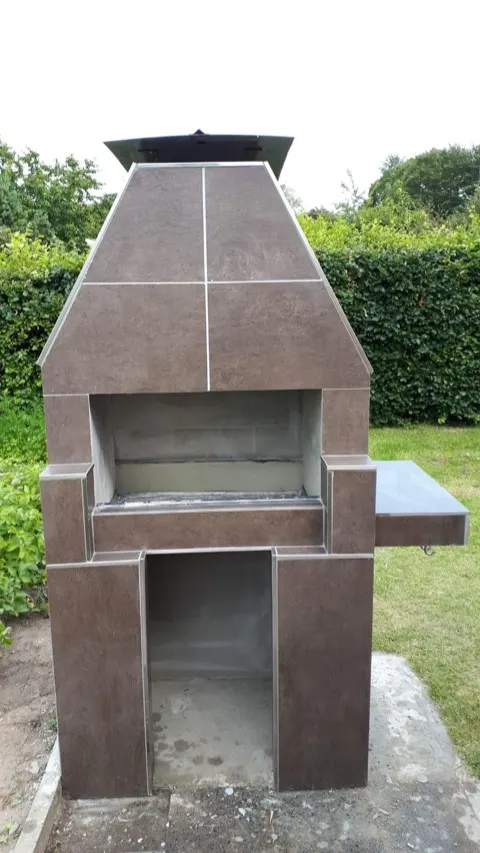 Fertig gebauter Grillkamin mit Fliesenverkleidung vor der Hecke